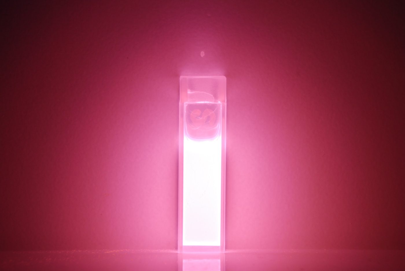 Cuvette of nanocrystal solution glowing pink under excitation