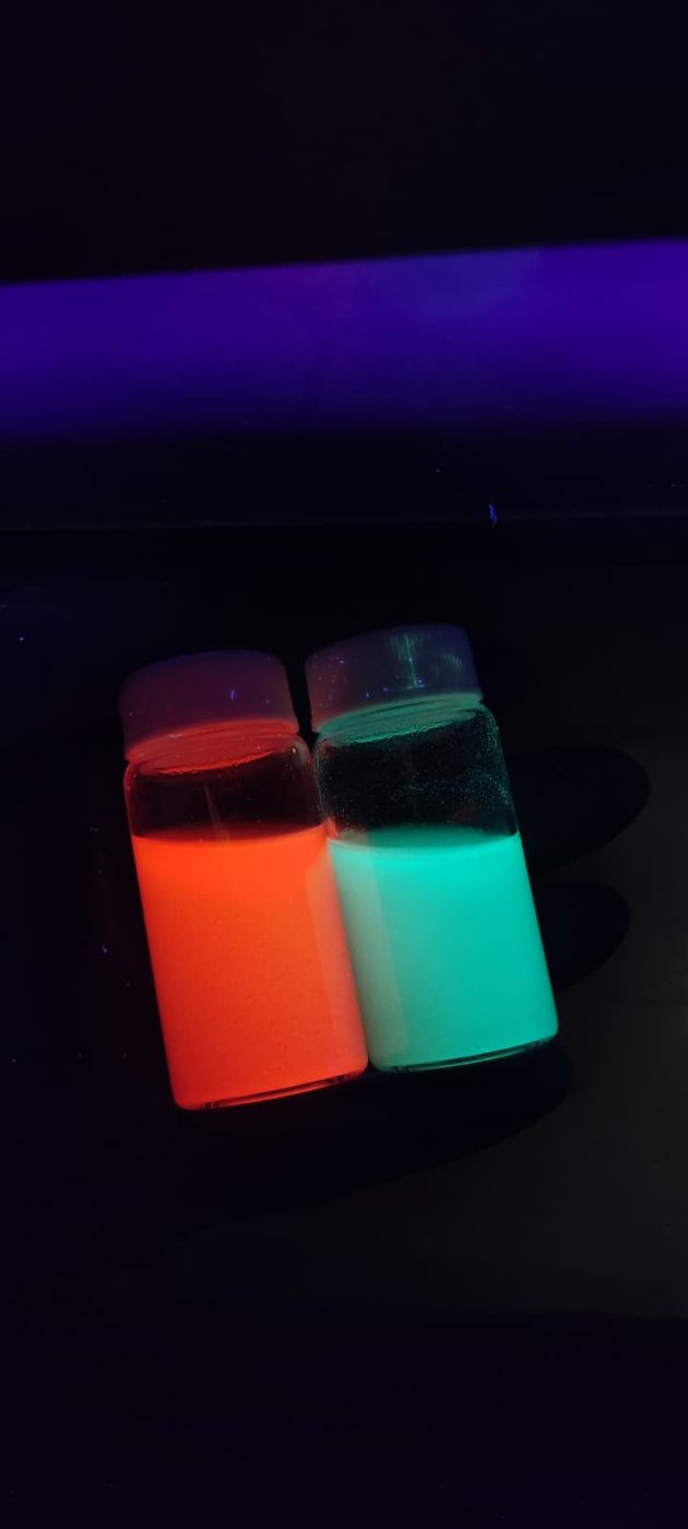 Two vials glowing orange and green under UV light